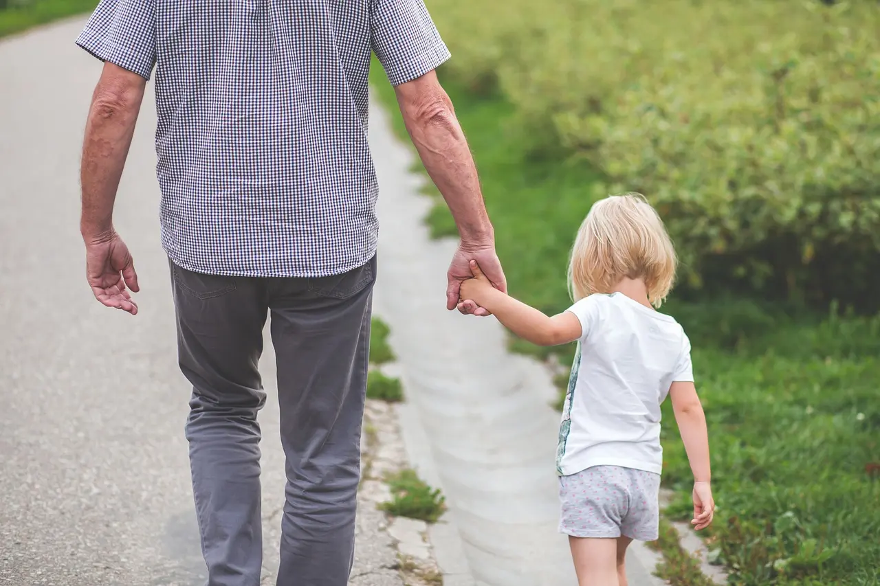 Un homme et un enfant de dos, marchent sur une route en se tenant la main.