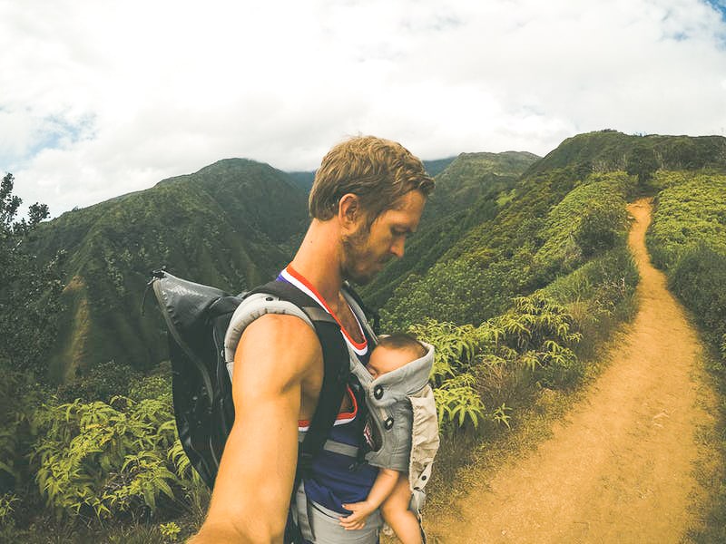 Père en voyage qui porte son enfant en bandoulière